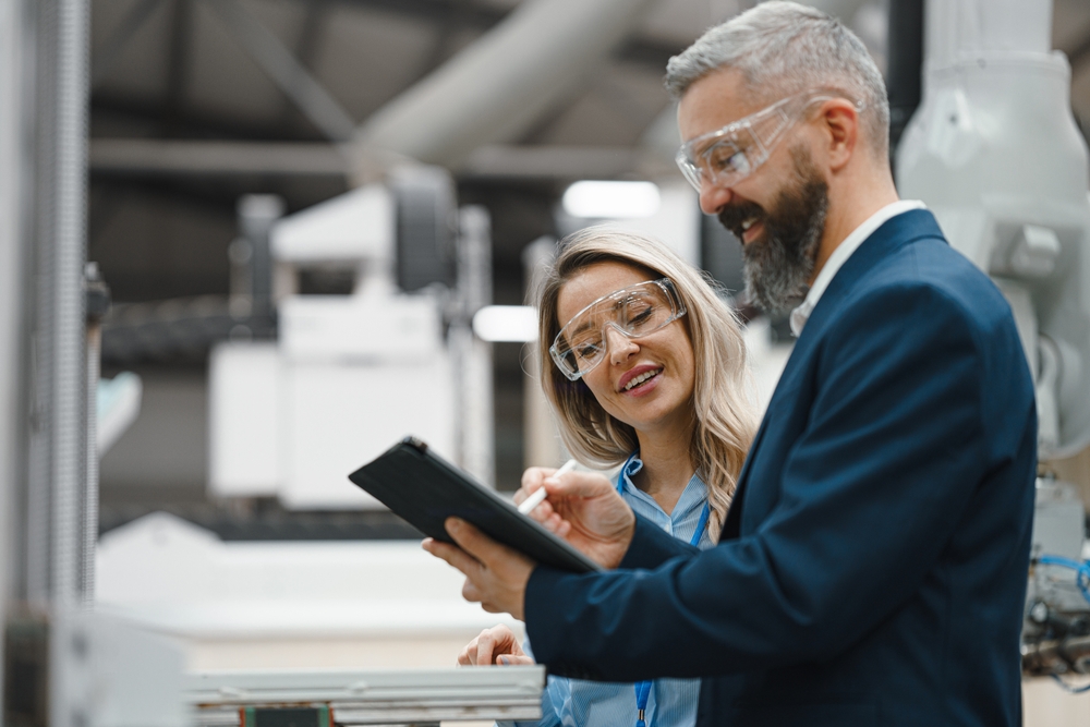 Female engineer and male production manager standing in modern industrial factory, talking about production. Manufacturing facility with robotics and automation.